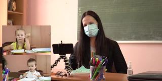 一个戴着防护面具的老师和小学生的虚拟在线会议。拼贴画在屏幕上