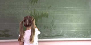 一个小女孩在黑板上用粉笔写字母。幼儿园education.4k