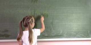 一个小女孩在黑板上用粉笔写字母。幼儿园education.4k