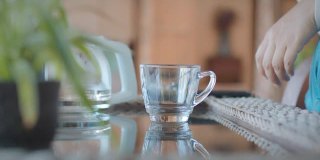 一名亚洲妇女，在家休息时将茶壶里的热水倒进带有干茶叶的杯子里。
