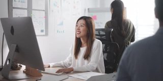 亚洲女商人与她的同事在办公室用电脑工作