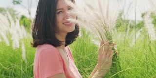 亚洲美丽的年轻女子的肖像站在绿色的草地草地草与微笑的脸。放松的女孩，心情愉快，享受假期的快乐时光。