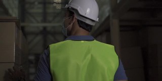 年轻的印度工厂仓库工人戴着防护面罩和安全帽在物流行业室内工作。30多名男子在检查新冠肺炎大流行期间的库存订单