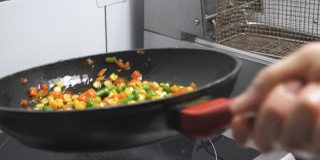 男厨师手拿平底锅，在厨房餐厅里翻炒各种蔬菜。用橄榄油煎炸玉米、豌豆、芦笋、胡椒和胡萝卜。烹饪食物的概念。
