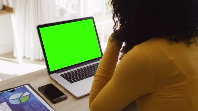 后视图的非洲裔美国妇女看笔记本电脑与绿色屏幕，而从家里工作