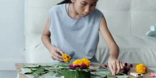快乐的亚洲女孩花插花(由香蕉叶和花漂浮在河里祈祷和感谢你)一起在家，为晚上的时间做准备。