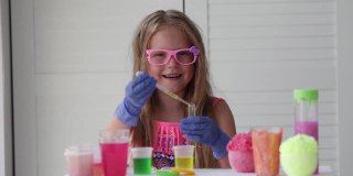 一个戴着粉色眼镜的小女孩做着实验，看着摄像机微笑着。一个戴着橡胶手套的孩子用吸管将一种黄色液体倒入试管中。实验。