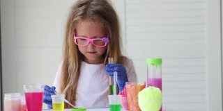 一个戴眼镜的小女孩正在玩自制的粉红色黏液。孩子们用手玩黏液玩具。使粘液。Copyspace。