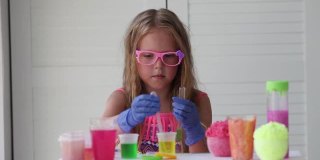 一个戴着粉色眼镜的小女孩做着实验，看着摄像机微笑着。一个戴着橡胶手套的孩子用吸管将一种黄色液体倒入试管中。实验。