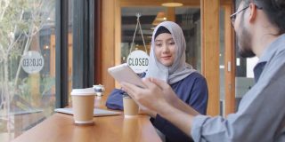 快乐多元的亚洲穆斯林年轻女子与朋友在咖啡馆会议上谈笑风生，多元文化开朗的人们围坐在café桌边喝咖啡