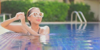 年轻的亚洲女人放松愉快周围的室外游泳池