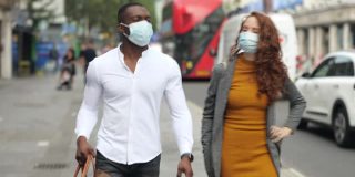一对夫妇戴着防护口罩走在繁忙的伦敦大街上