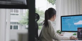 宽镜头的年轻迷人的亚洲女人忙着工作的多屏幕电脑和智能平板电脑在桌子上在家里的概念自由职业者数据分析师，数据科学家的业务。