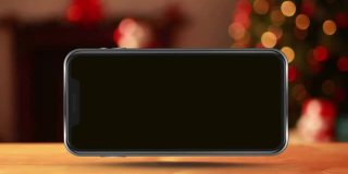 木制表面智能手机屏幕上显示圣诞快乐文字和童话灯的动画
