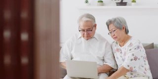 亚洲老年夫妇在家中客厅使用电脑笔记本上网搜索、网上购物、购买保险，老年人具有科技理念