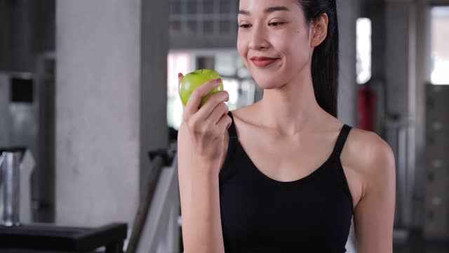 亚洲美女在健身房咬青苹果的肖像。