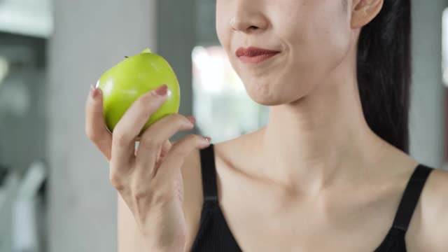 特写亚洲美丽的女人在健身房咬青苹果。