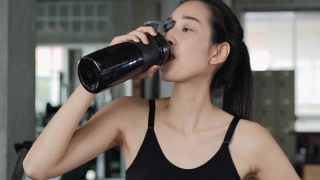 亚洲美女在健身房喝水的肖像。
