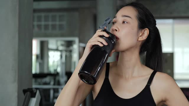 亚洲美女在健身房喝水的肖像。