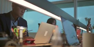 亚洲华裔年轻商人在办公室里工作，在他的工作场所用笔记本电脑做他的报告