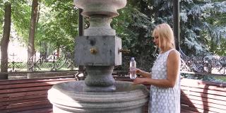 年轻女子从源头喝瓶装水。水泵配备户外矿泉水
