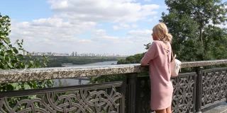 一个女人站在桥上，用一条河看着城市风景