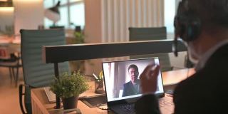 成熟的亚洲华人商人留着胡子，在办公室用笔记本电脑与客户视频通话