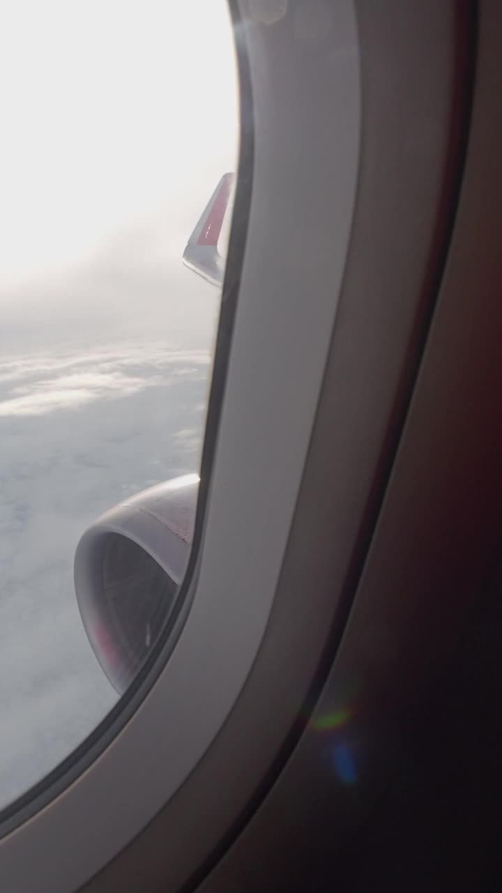 从窗口看，飞机喷气发动机在飞行中工作。旅行时从飞机窗口望出去看天空。探索和旅程的概念。垂直视频。