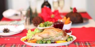 感恩节或圣诞节晚餐的餐桌女人用手放了一个盛着食物的盘子。前景是塞满馅的烤火鸡。庆祝传统节日