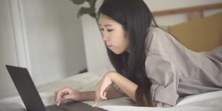 亚洲美女躺在床上，在卧室里使用笔记本电脑。