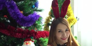 亚洲美丽的年轻女子在性感的红色内衣和兔子耳朵坐在白色的床上圣诞树的背景。性感的小兔子的女孩