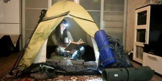 一个女孩戴着医用口罩在一间公寓的露营帐篷里看书。闭关锁国则在家里摧毁。冠状病毒大流行。怀念旅行和远足