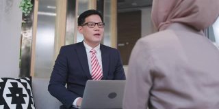 亚洲商人穿蓝色西装坐着协商或向同事介绍工作。头脑风暴的工作将完成这个项目。在办公室用笔记本电脑进行商业和金融投资。