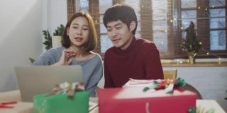 快乐的亚洲夫妇与视频通话，同时使用笔记本电脑和打开圣诞礼盒