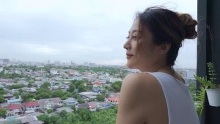 年轻美丽的亚洲女人在早上站在公寓阳台上，欣赏大都市的城市景观建筑的景色。2019冠状病毒病大流行封锁和心理健康概念。视频素材模板下载