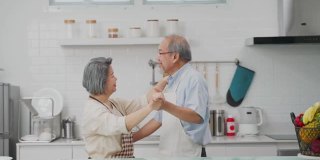 夫妇老亚洲长者幸福生活在家庭厨房。爷爷奶奶跳着幸福的舞蹈，微笑着享受退休生活。老年人的家庭关系和活动概念。