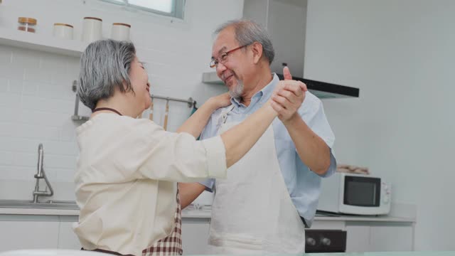 夫妇老亚洲长者幸福生活在家庭厨房。爷爷奶奶跳着幸福的舞蹈，微笑着享受退休生活。老年人的家庭关系和活动概念。