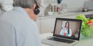 亚洲资深男士在家客厅与医生视频通话。病人老人咨询全科医生应用电脑。医生和顾问在线和远程医疗的概念。