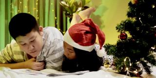 快乐的亚洲孩子们在晚上一起看书和躺在床上，用圣诞装饰的时间，生活理念。