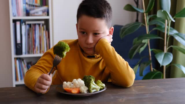 孩子对不得不吃蔬菜很不高兴。他的盘子里有许多蔬菜。他讨厌蔬菜。