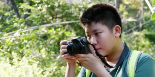 亚洲男孩学习使用相机如何拍摄以自然为背景，冒险的概念。