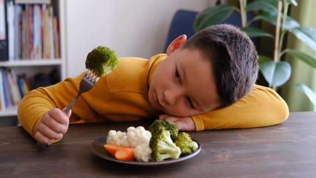 孩子对不得不吃蔬菜很不高兴。他的盘子里有许多蔬菜。他讨厌蔬菜。