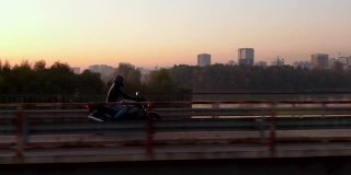 航拍的摩托车手在傍晚的路上骑摩托车。电影拍摄的摩托车在日落道上的桥。观沿河驾驶的电单车。概念的自由生活方式