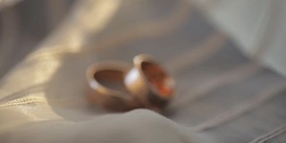 两个金色的结婚戒指躺在白灰色的表面上，在近距离的微距下闪闪发光