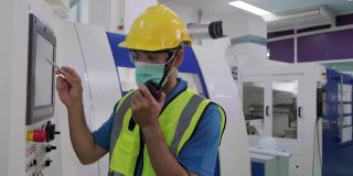男工程师/工人用对讲机与工厂的技术人员沟通，咨询机器的问题。他戴着防护口罩，以保护烟尘和COVID-19病毒