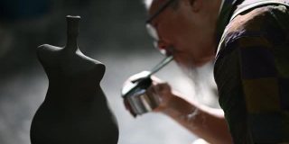 亚洲华人高级泥塑艺术家在雕塑家身上吹颜料，在他的工作室里用纺纱陶轮工作