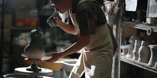 亚洲华人高级泥塑艺术家在雕塑家身上吹颜料，在他的工作室里用纺纱陶轮工作