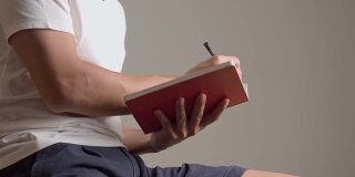 一名身穿白色t恤的亚洲男子用钢笔和笔迹在红纸笔记本上记下讲师的笔记。孤立的背景。