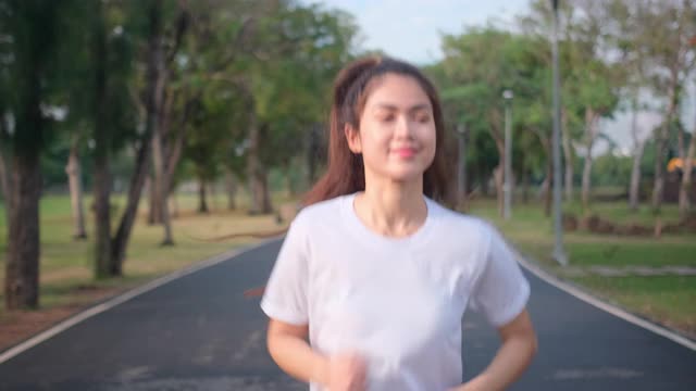 亚洲女运动员的肖像是在绿色公园的道路上慢跑，带着傍晚的光和快乐的情绪微笑