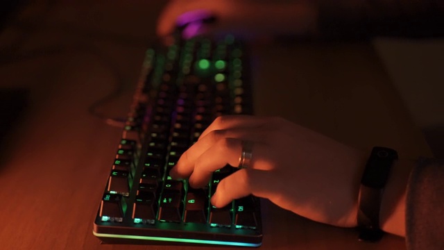 玩家双手敲击电脑键盘，RGB背光照明，专业视频游戏玩家花时间在家里玩虚拟网络游戏。Pro cyber sport gamer概念
